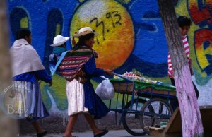 A mom in La Paz Bolivia carries her baby while pushing a cart