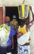 A mom in West Africa carries her baby on her back and bucket on her head