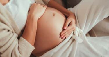 pregnant woman laying in bed holding her growing tummy