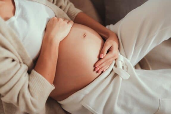 pregnant woman laying in bed holding her growing tummy