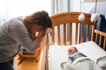 mom leaning over crib tired while baby cries