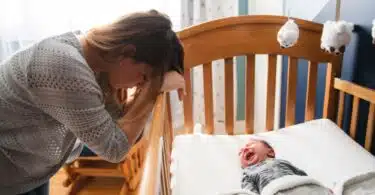 mom leaning over crib tired while baby cries