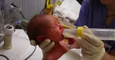 tiny preemie being fed breast milk by a nurser in NICU