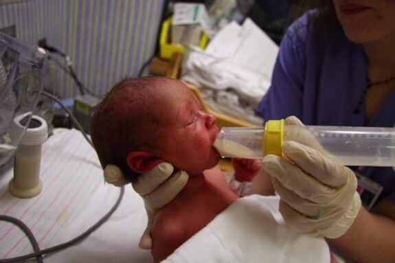 tiny preemie being fed breast milk by a nurser in NICU