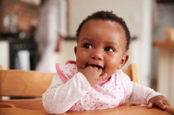 baby with brown skin eating food with its hands