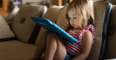 toddler sitting on a couch watching an ipad