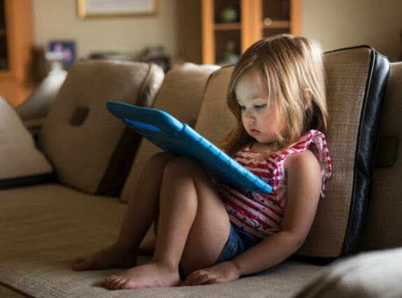 toddler sitting on a couch watching an ipad