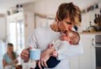 Young father holding a newborn baby in kitchen at home, kissing.