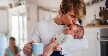 Young father holding a newborn baby in kitchen at home, kissing.