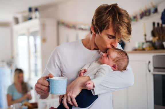 Young father holding a newborn baby in kitchen at home, kissing.