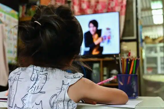 close up Schoolgirl learning online sitting on floor and watching television 
