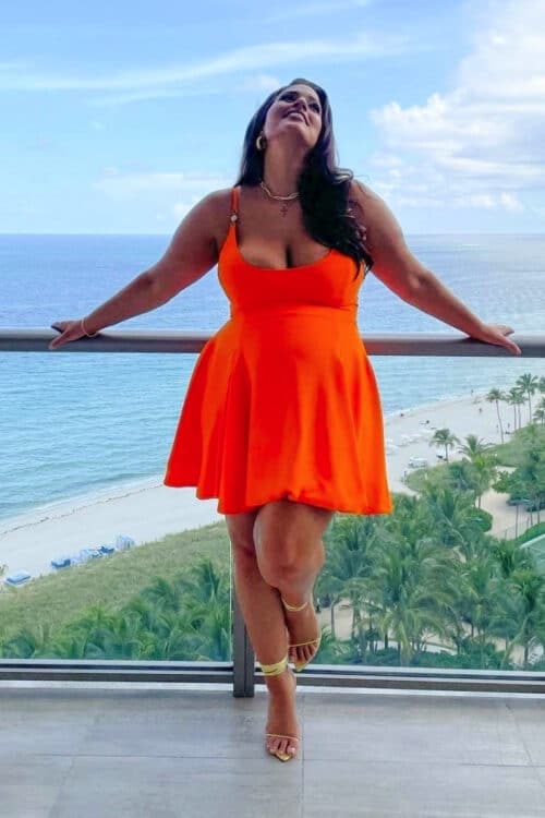 Pregnant Ashley Graham poses on her hotel balcony for Revlon Press in a Versace dress