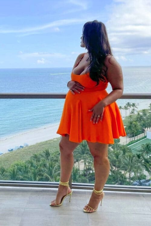 Pregnant Ashley Graham poses on her hotel balcony for Revlon Press in a Versace dress