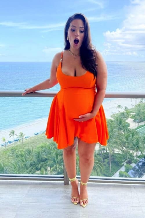 Pregnant Ashley Graham poses on her hotel balcony for Revlon Press in a Versace dress in Miami