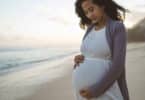pregnant woman looking down at her belly while standing at the beach