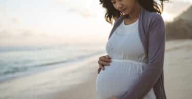 pregnant woman looking down at her belly while standing at the beach