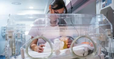 Female doctor examining newborn baby in incubator