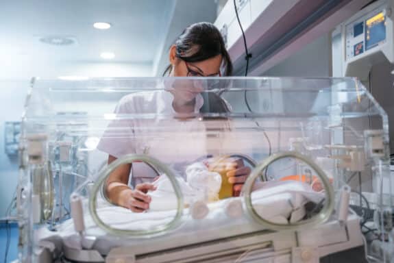 Female doctor examining newborn baby in incubator