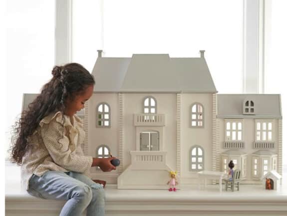 little girl sitting beside her grey and white dollhouse