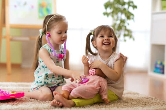 two girls play with a baby doll