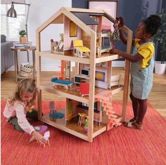 two kids play with a tall wooden dollhouse