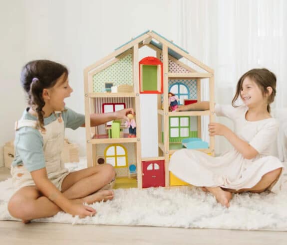 two girls play with wooden dollhouse
