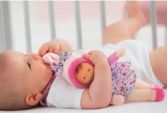 baby lying in crib with baby doll