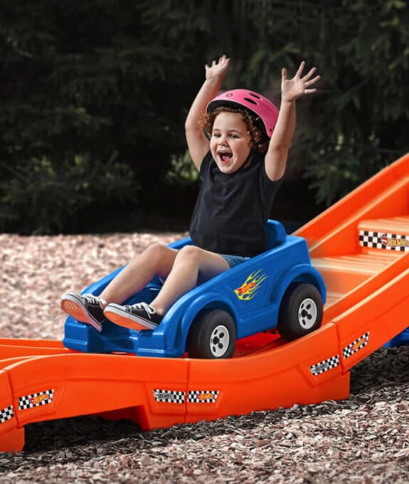 toddler with his hands up as he rides down a plastic roller coaster