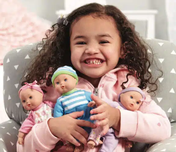 little girl holding 3 dolls smiling