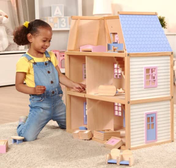 a young girl playing with the inside of a wooden dollhouse