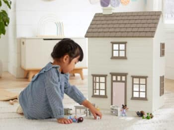 little girl playing in front of her wooden dallhouse