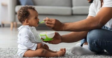 Father Feeding His Adorable Infant Baby Son With Spoon