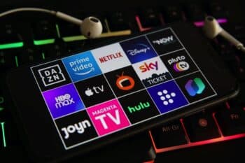Closeup of mobile phone screen with logo lettering of various tv movie streaming services on laptop keyboard