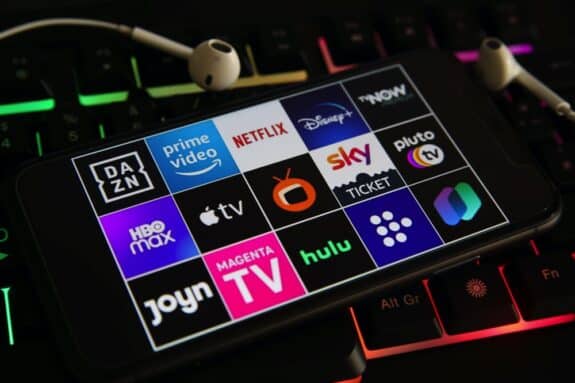 Closeup of mobile phone screen with logo lettering of various tv movie streaming services on laptop keyboard