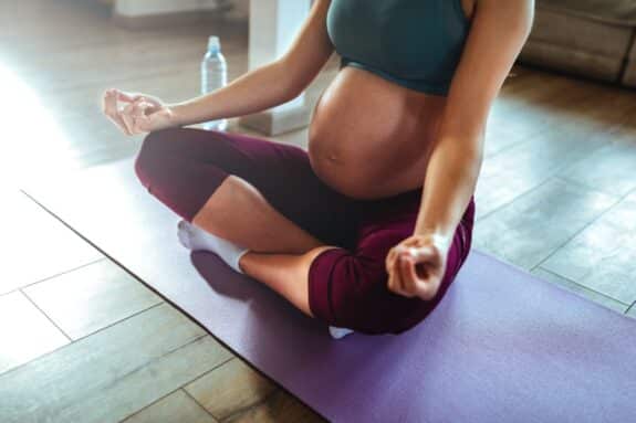 fit pregnant african american woman doing yoga on gray mat in her living-room