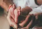 small feet of a newborn supported by the hand of his father