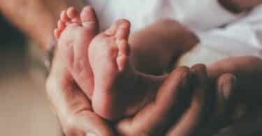 small feet of a newborn supported by the hand of his father