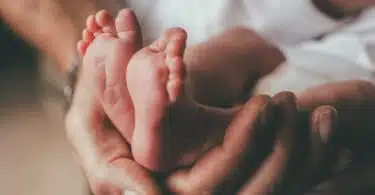 small feet of a newborn supported by the hand of his father