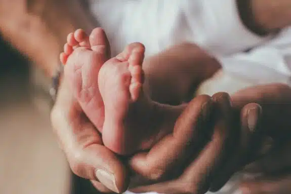  small feet of a newborn supported by the hand of his father 