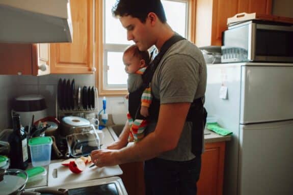 father with newborn baby in carrier preparing lunch.