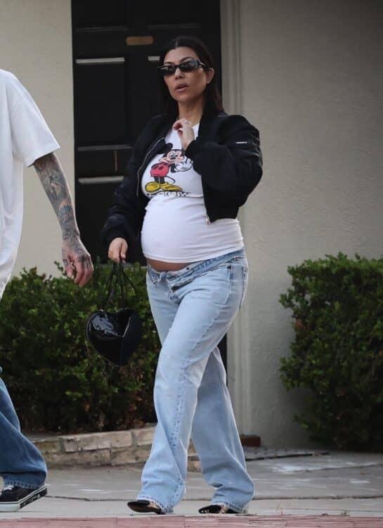 Pregnant Kourtney proudly displaying her growing belly under a vintage Mickey Mouse flipping the bird t-shirt, ripped jeans and bonnet jacket combo