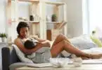young black mom sitting on sofa bed and breastfeeding baby while holding son in arms