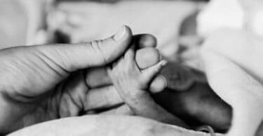 parent holds the tiny hand of their premature baby