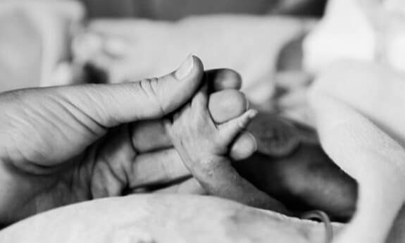 parent holds the tiny hand of their premature baby