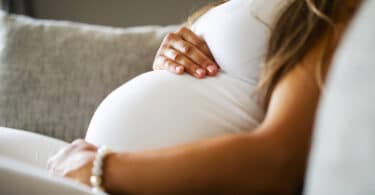 Close-up of pregnant woman sitting in sofa with her hands at belly
