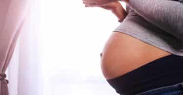 Pregnant woman stand by the window and drink tea