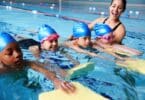 Coach In Water Giving Group Of Children Swimming Lesson In Indoor Pool